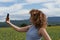 Portrait of beautiful happy Caucasian girl making selfie photo on smartphone while standing in golden field.