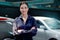 Portrait of beautiful happy smiling female auto mechanic in uniform standing arms crossed near vehicle at garage, technician woman