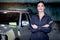 Portrait of beautiful happy smiling female auto mechanic in uniform standing arms crossed near vehicle at garage, technician woman