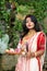 Portrait of beautiful Indian Bengali female model in ethnic saree and jewellery holding plate of religious offering