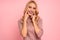 Portrait of beautiful joyous woman smiling and touching her face with fingers isolated over pink background in studio