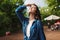 Portrait of beautiful lady with wet hair in denim shirt dreamily closing her eyes while standing under rain in park