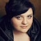 Portrait of a beautiful large girl in a black dress with a seductive decollete posing over light-brown background. Close up. Stud