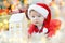 Portrait of beautiful little baby celebrates Christmas. New Year`s holidays. Boy in a santa costume with toy house under the tree