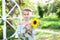 Portrait of beautiful little girl with pigtail on her head holds sunflower. Childhood concept. Teenager girl with sunflower in gar