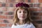 portrait of a beautiful little girl wearing a red crown roses on her head. Brick background. Lifestyle
