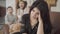 Portrait of a beautiful Middle Eastern mother with migraine sitting on the armchair and her two little children jumping