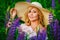 Portrait of a beautiful plump blonde in a large straw hat, a girl with a bouquet of lupines in her hands, posing in a blooming