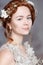 Portrait of beautiful red-haired bride. She has a perfect pale skin with delicate blush. White flowers in her hair.