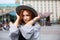 Portrait of beautiful red-haired girl in a grey coat and hat walks through the city