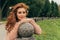 Portrait of a beautiful, red-haired girl who leaned her elbows on a granite ball in the park, the wind develops her curls, beautif