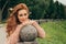 Portrait of a beautiful, red-haired girl who leaned her elbows on a granite ball in the park, the wind develops her curls, beautif
