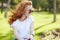 Portrait of a beautiful red-haired girl who sits in the park and looks away. The wind develops her hair and the girl smiles