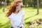 Portrait of a beautiful red-haired girl who sits in the park and looks away. The wind develops her hair and the girl smiles