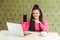 Portrait of beautiful satisfied happy young businesswoman with black dreadlocks in pink blouse is sitting in cafe, holding phone