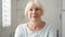 Portrait of beautiful senior blond woman at home. Sitting in white living room looking at camera