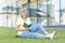 Portrait of a beautiful senior woman. Sitting on the grass, reading a book near a modern building, rests, has a good time