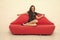 portrait of a beautiful sensual woman. relaxed girl sitting on red sofa. sexy model on leather couch. beautiful