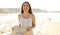 Portrait of beautiful smiling carefree woman walking on the beach in white dress holding straw hat looking at camera with