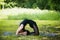 Portrait of beautiful smiling sporty fit blond young woman doing bikram yoga backbend on summer day, Natarajasana, full