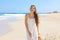 Portrait of beautiful smiling woman with white sundress walking on sand in empty wild beach on Canary Islands