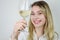 Portrait of a beautiful smiling young blonde woman who raises a glass of white wine to show its color and nuances