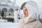 Portrait of beautiful smiling young Muslim woman in headscarf in light clothing against the background of mosque in the winter