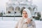 Portrait of beautiful smiling young Muslim woman in headscarf in light clothing against the background of mosque in winter season