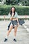 Portrait beautiful sportive Asian female skater wearing hipster clothes with lollipop, smiling with happiness, holding skateboard