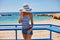 Portrait of beautiful tanned woman at the sea coast in hat and retro style clothes. Hot summer day and bright sunny light.