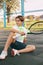 Portrait of a beautiful teenage boy with a tennis racket in his hands. A tennis player sits on the court and rests after