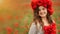 Portrait of a beautiful teenager girl in a wreath of poppy flowers looking smiling, on a green field with a bouquet of poppies in