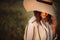 Portrait of beautiful woman in hat enjoying sunset golden light in summer meadow. Stylish rustic girl in linen dress relaxing in