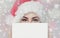 Portrait of a beautiful woman in a red Santa Claus hat and knitted red sweater holds in her hand a white sheet of paper for the i