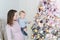 Portrait of beautiful young adult caucasian woman wiht cute adorable little blond toddler boy enjoy trimming christmas tree in