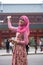 Portrait of beautiful young Asian muslim woman at gate of shrine in Japan waving hand and holding smart phone. Happy expression.