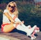 Portrait of a beautiful young blonde girl tighten the laces sitting on a bench in a vintage roller skates, sunglasses wearing shor