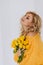 Portrait of a beautiful young blonde woman with a bouquet of yellow roses in a voluminous sweater on a white background in the