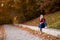 Portrait of beautiful young brunette woman in red shirt and jeans hiding eyes behind autumn leaves