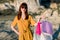 Portrait of beautiful young Caucasian woman in sunglasses and yellow overalls, smiling with shopping bags outside