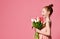 Portrait of a beautiful young girl in dress holding big bouquet of irises and tulips isolated over pink background