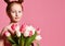 Portrait of a beautiful young girl in dress holding big bouquet of irises and tulips isolated over pink background