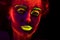 Portrait of a beautiful young girl with ultraviolet paint on her body and glowing contact lenses looking in camera