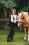 Portrait beautiful young girl in white shirt and black pants with beauty long hair next horse in forest. Fashionable elegance woma