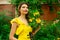 A portrait of a beautiful young musician girl in yellow dress with a violin in hand. Green plants, yellow flowers and wooden