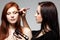 Portrait of beautiful young redheaded woman with esthetician making makeup eye shadow