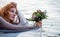 Portrait of beautiful young sexy red-haired girl with a longing, Lady of Shalott, with a bouquet of flowers in a boat, copy space