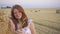 Portrait of a beautiful young smiling girl near the round bale of hay in a wheat field