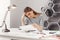 Portrait of beautiful young unhappy female engineer sitting at white table in cosy coworking space, looking at papers