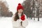 Portrait of beautiful young woman in red knitted hat and mittens and woolen sweater on alley in winter park